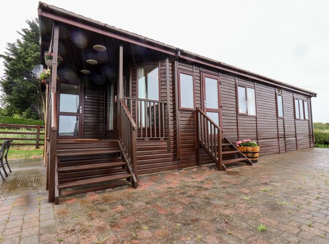 Exterior view of a wooden cabin with two sets of stairs and flower pots on a paved area at Handale Banks Farm Lodge in Liverton