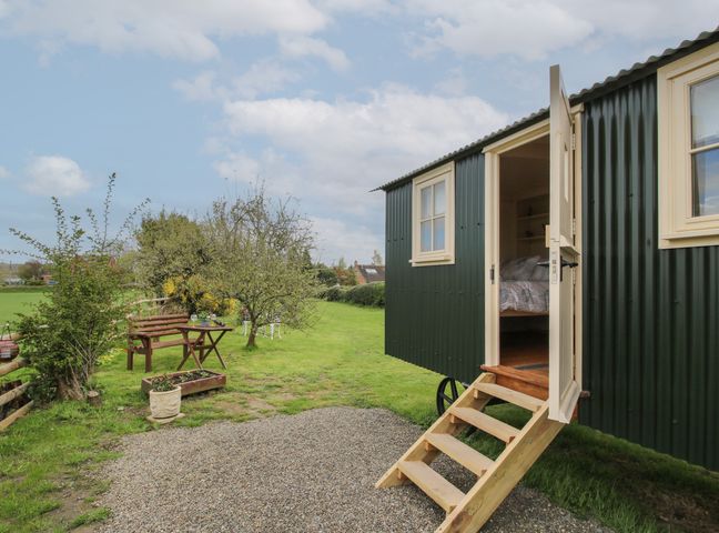A small green caravan with open door and wooden steps on grass with a wooden bench and table nearby at Le Petite Pound House in Bewdley