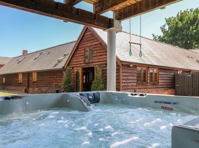 An outdoor hot tub with water jets in front of a wooden house with a sloped roof at Awelfan in Tregynon near Bettws Cedewain