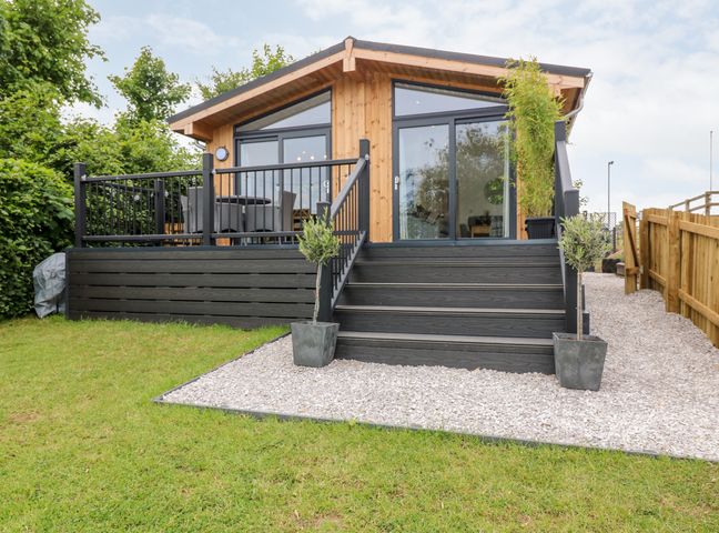 A wooden lodge with a black deck and stairs leading to the entrance surrounded by grass and gravel at Eden Fields Lodge in Cupar Fife