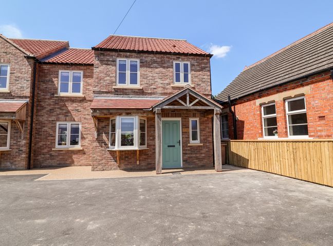 A brick house with a green door and a wooden porch with tiled roof at Keepers Cottage in Newton upon Derwent near Wilberfoss