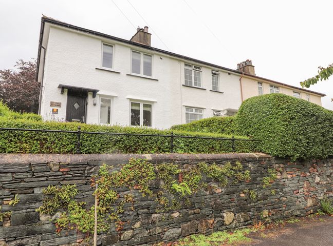 A row of white houses with black doors behind a stone wall and green hedges at 1 Millbank in Keswick