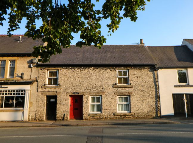 A stone facade house with a red door and four windows along a street at Wilson Eyre Cottage in Castleton Peak District