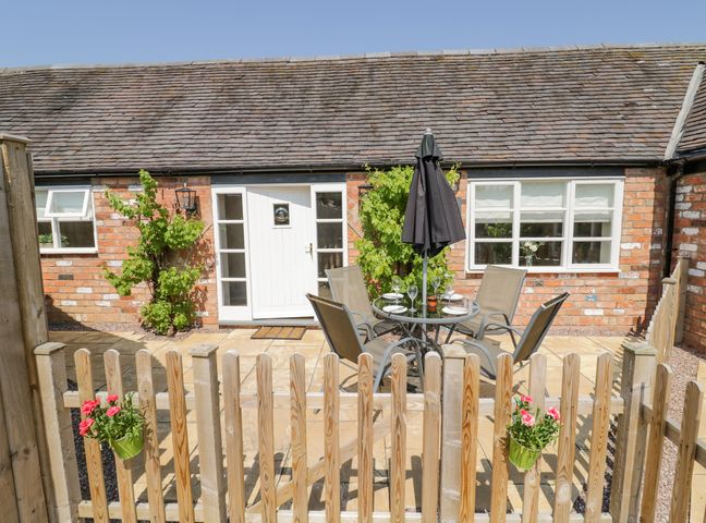 A small fenced patio area with a table and four chairs in front of a brick building with white door and windows at The Nest in Sutton Cheney near Market Bosworth
