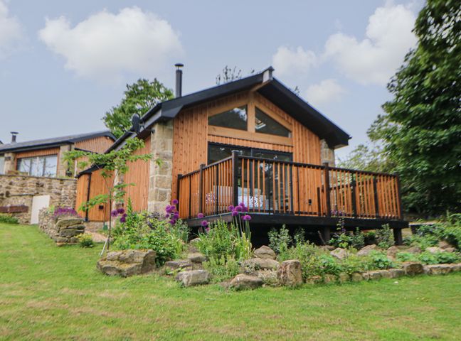 A wooden house with a deck and garden with flowers in front at The Bothy Riding Hills Riding Mill near Corbridge