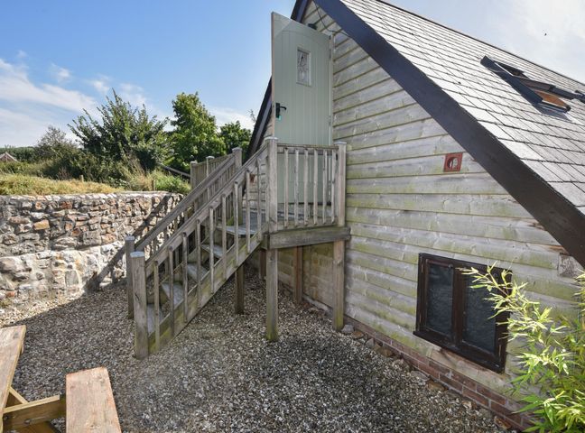 Exterior side view of a wooden house with a small staircase leading to an elevated door at Brookhaven in Musbury