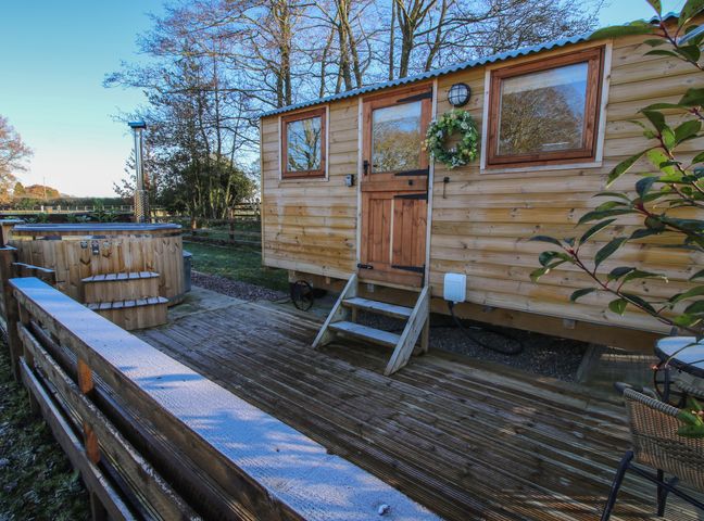 An outdoor wooden deck with a hot tub and a wooden cabin with a door and windows at The Oak Hut in Coton near Whitchurch