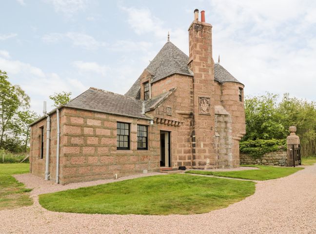 An exterior view of a stone house with multiple roofs a chimney and grassy area at Holly Leaf Cottage Drum Castle Estate Drumoak near Peterculter