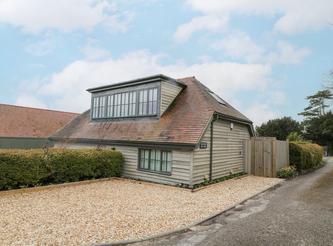 A barn-style house with a gravel driveway and hedges along a road at Little Barn in Stockbridge