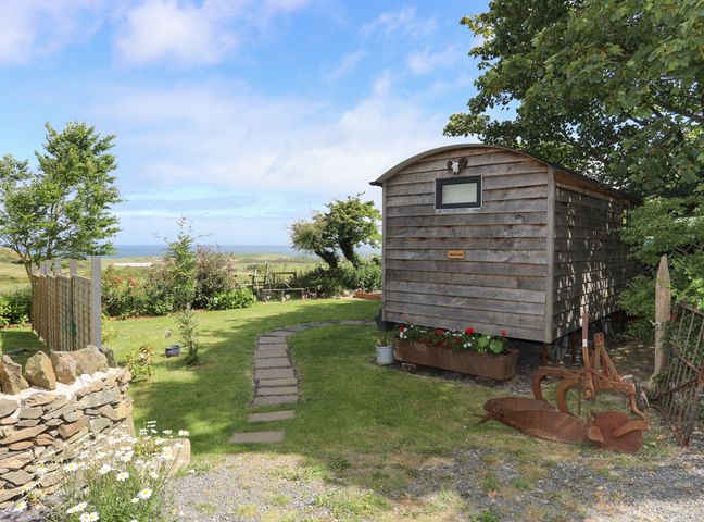 A garden area with a wooden shed flowers on the ground a stone wall and distant ocean view at Shepherds Stone Llanfairynghornwy near Llanfaethlu