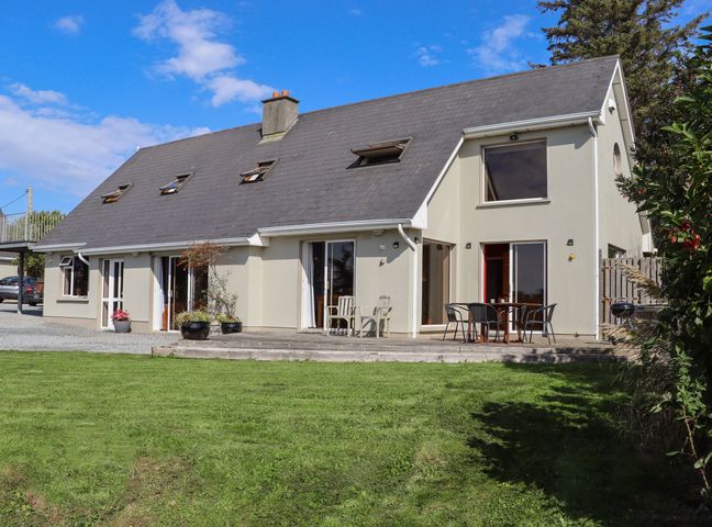A modern two-story house with multiple windows and doors a patio with outdoor chairs and tables and a green lawn at Seafield in Ballymoney County Wexford