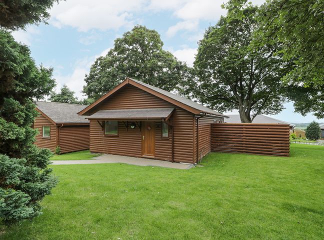 A brown wooden cabin with a small porch and surrounding green lawn at Luxury Lodge 69 in Dyserth