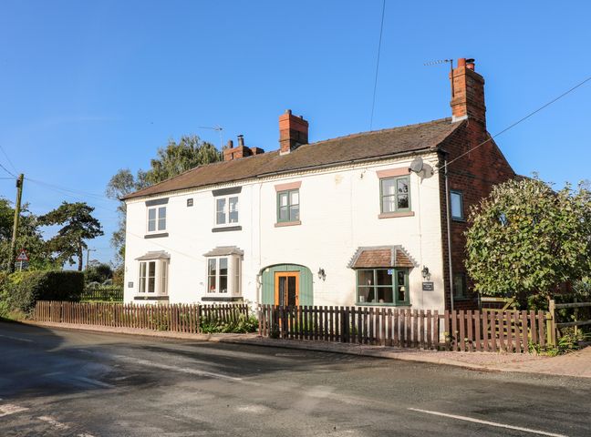 A two-story white brick house with green trim windows and a wooden fence along the street at Bluebell Cottage Bellamour near Rugeley