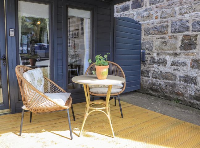 An outdoor patio with two wicker chairs with cushions a round table with a potted plant on a wooden deck at Creed Cabin in Stornoway