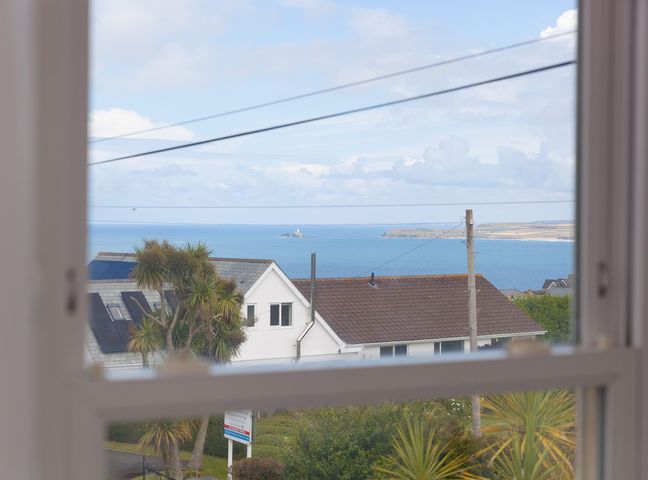 A coastal view through a window showing houses palm trees power lines and the sea at Samphire in Carbis Bay