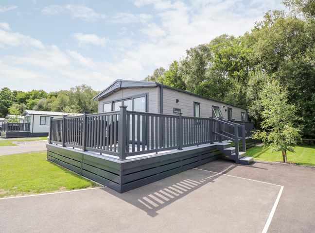 A gray mobile home with a raised deck and steps surrounded by grass and trees at 7 Wild Haven in Landford