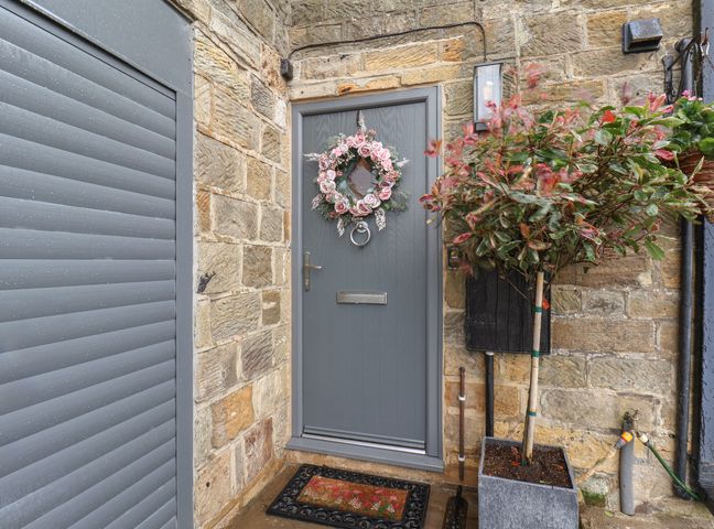 A stone entryway with a gray door decorated with a wreath next to a potted tree at Brambles Apartment Sneatonthorpe near Ruswarp