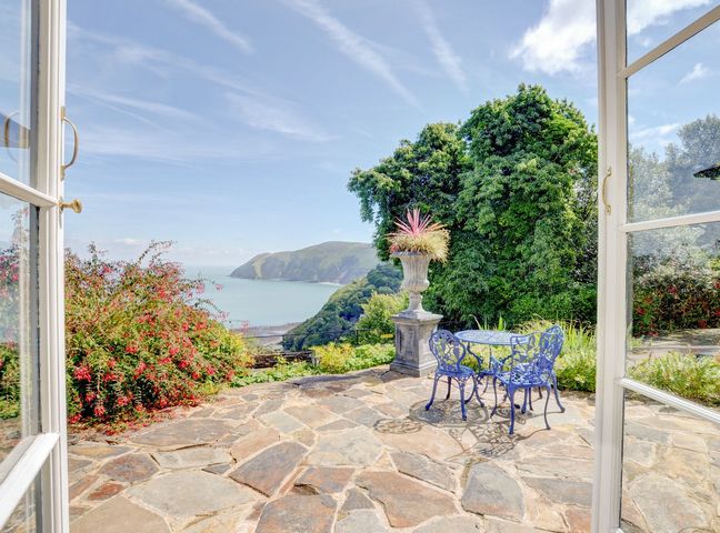 A stone patio with a metal table and chairs and ocean view at Baronet's Quarters in Lynton