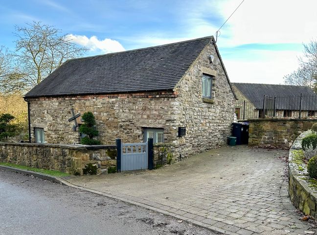 A stone building with a slate roof next to a paved driveway and a low stone wall at Lilimae Barn in Hognaston near Hulland Ward