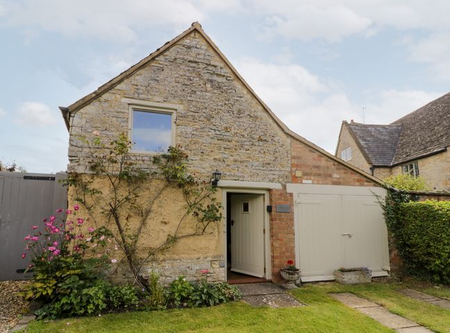 A stone cottage with a white wooden door and window surrounded by flowers and greenery at Old Bothy in Halford