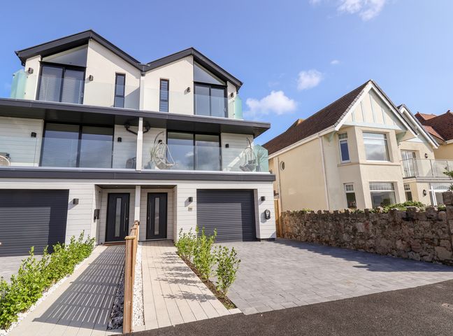 A modern two-story house with balconies, glass railings, garages, and a driveway at The Dunes in Llandudno