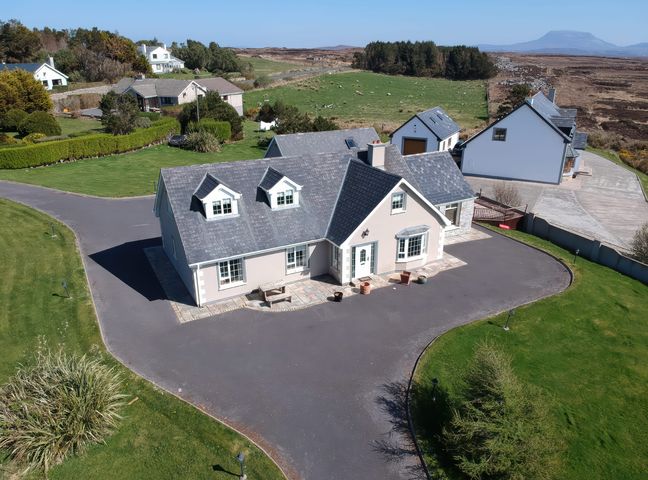 A large house with a paved driveway and green lawn surrounded by other houses and open fields at Gweedore View House in Derrybeg County Donegal