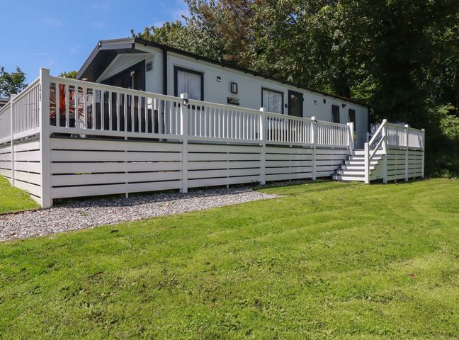 A white fenced deck attached to a single story building with grass and trees at Pams Place in Crantock