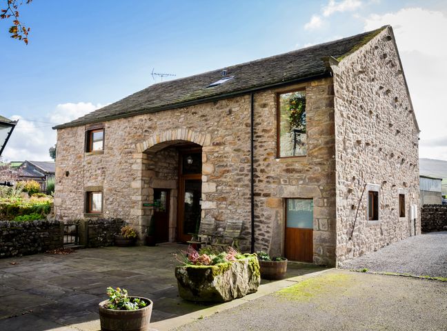 A stone building with wooden doors and windows and planters outside at Linton Laithe in Linton near Threshfield