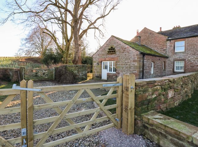 A stone house with a wooden gate and a gravel driveway surrounded by stone walls at Luham Cottage Edenhall near Langwathby