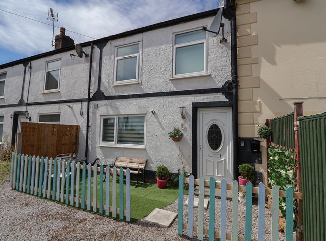 A small garden area with a wooden bench table and chairs behind a blue picket fence in front of a white and black house at 2 Stoneleigh Cottage Summerhill near Gwersyllt