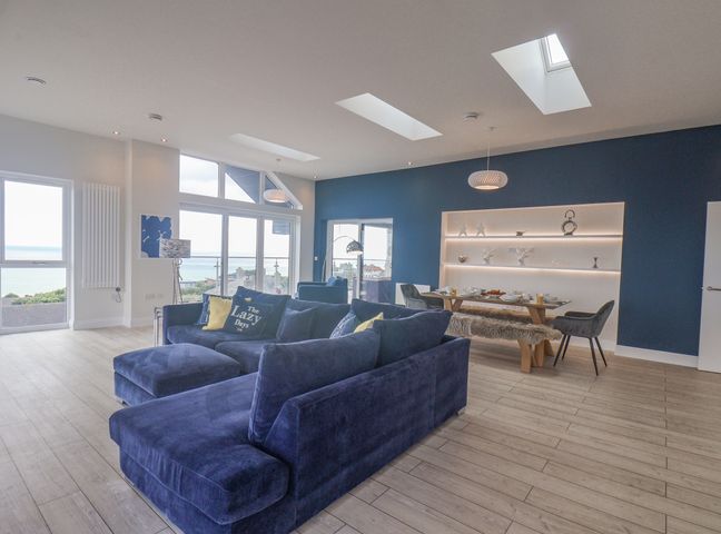 A living room with a blue sofa near a dining table with chairs and decorative shelves at The Penthouse in Scarborough