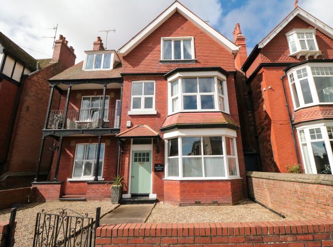 A red brick residential building with white windows a green door and a small front garden at North Bay View in Bridlington