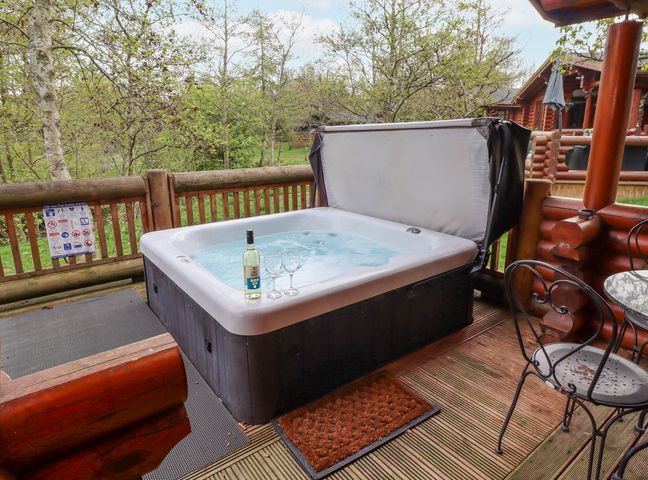 An outdoor hot tub with a bottle of wine and two glasses on the edge on a wooden deck with a metal chair at 24 Lakeside Drive in Felton
