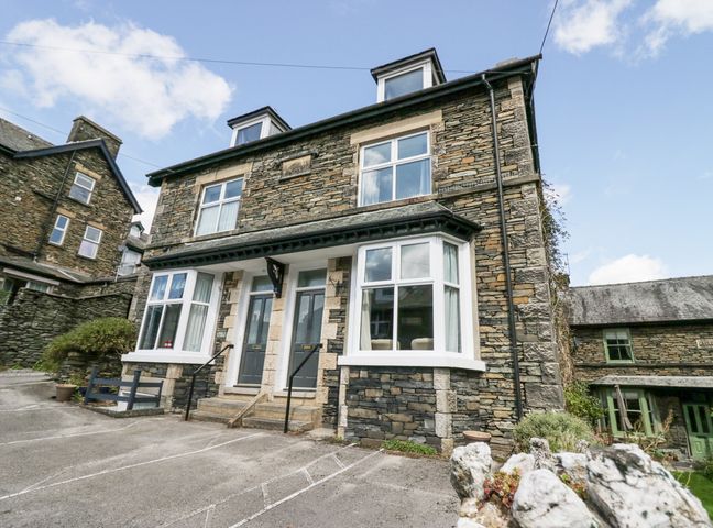 A stone house with two front doors and bay windows with parking spaces in front at Park Beck in Windermere