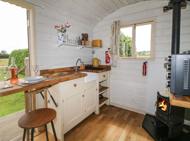 A small kitchen with wooden countertops a sink a window a stove with fire and an open door at Floras Hut in Liskeard