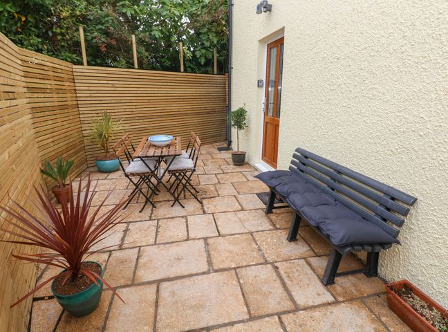 A patio area with a wooden table and chairs a bench with cushions and potted plants at The Loft @ Wisteria Cottage in Saundersfoot
