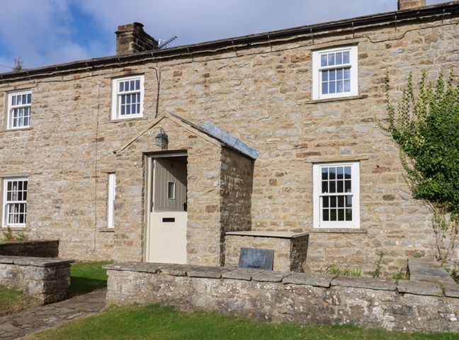 An exterior view of a stone cottage with a small porch and white framed windows at Pheasant Cottage in Reeth