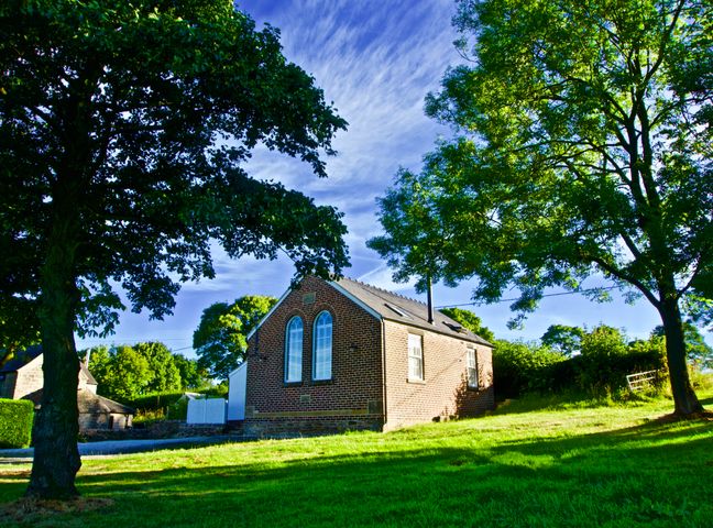 A small brick building with arched windows surrounded by trees and grass at The Chapel in Brackenfield near Stretton Derbyshire