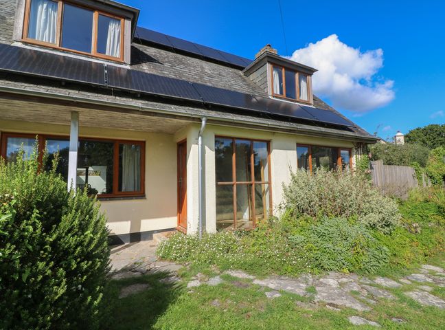 A cream house with wooden windows and solar panels on roof surrounded by greenery at Mulberry Cottage in Staple near Dartington