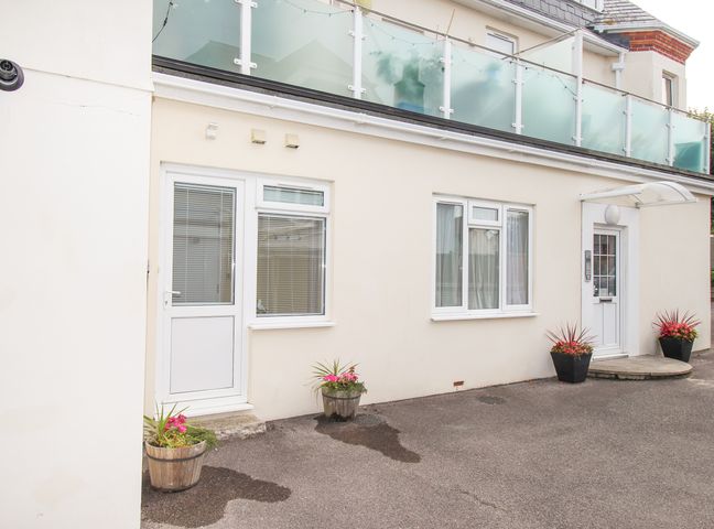 An exterior view of a building with a door and windows and flower pots at the entrance at Sandy Haven in Swanage