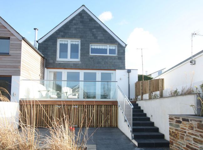 An exterior view of a two-story house with a balcony and outdoor chairs at The Beach House in Polzeath