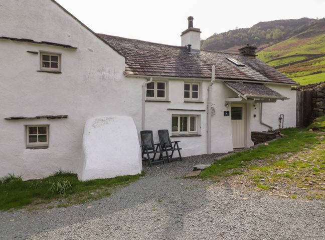 An exterior view of a white cottage with a tiled roof and two black chairs outside at Two Side House Farm in Langdale