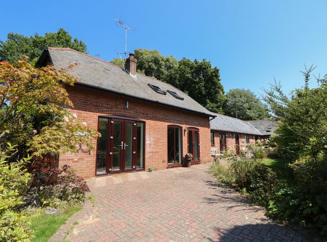 A brick building with multiple windows and doors surrounded by plants and trees at Northern Byre in Sopley