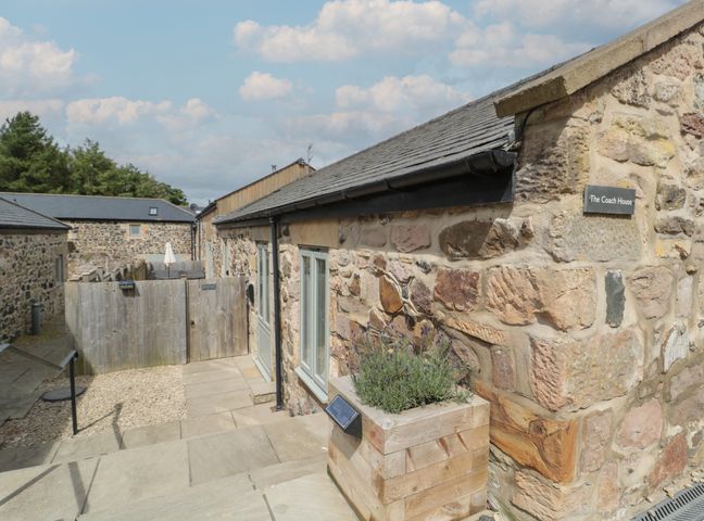 Stone building exterior with wooden planter and fenced patio area at The Coach House in Bamburgh