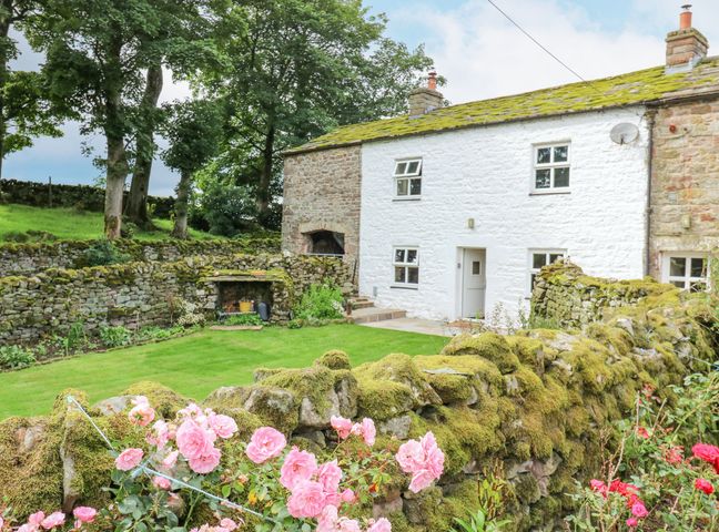 A stone cottage with a mossy roof and garden with pink flowers and stone walls at The LA'AL Cragg in Kirkby Stephen