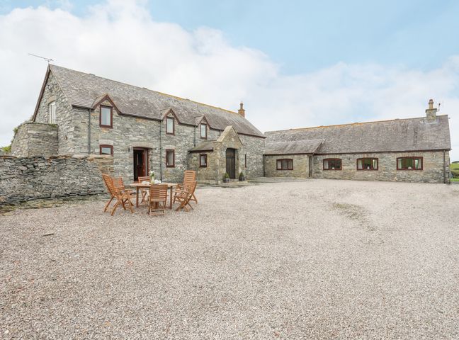 A stone house with multiple windows and a gravel courtyard with wooden table and chairs at Caerdegog Ganol in Cemlyn near Cemaes Bay