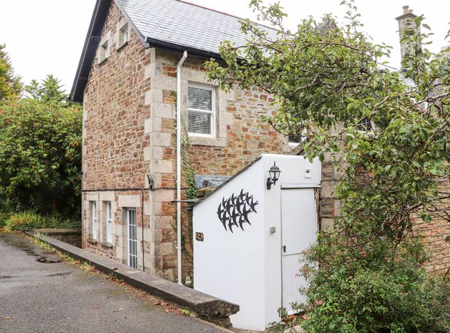Stone house with a white side entrance and metal bird decoration surrounded by greenery at Little Polgray in St Austell