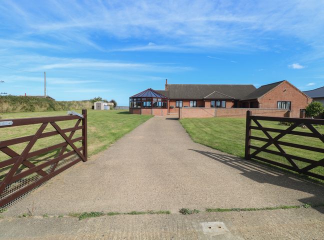 A driveway leading to a brick house with a conservatory and two wooden gates open at Beach Haven in Happisburgh East Anglia