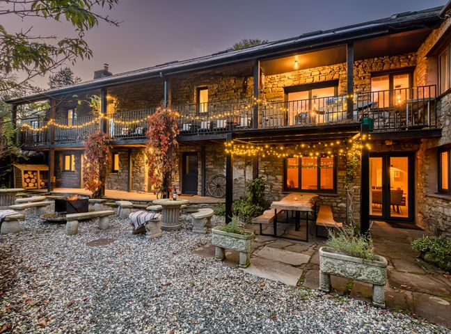 An outdoor patio area with string lights stone benches a fire pit and a wooden table at The Waterfall Retreat in Orton