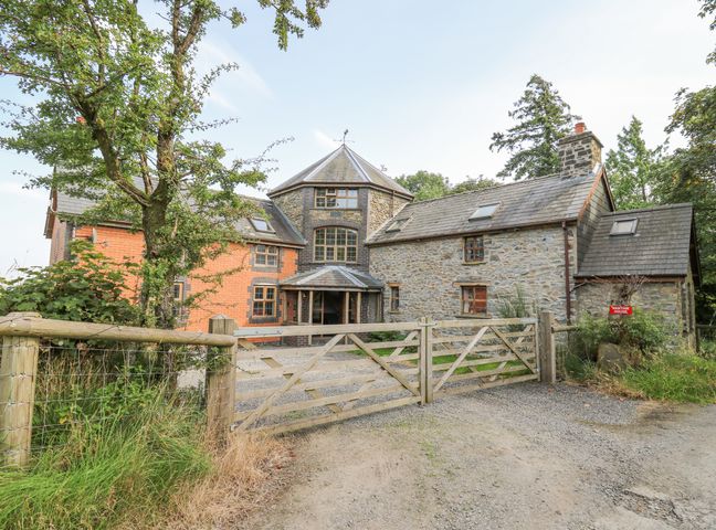 The exterior of a stone and brick house with a wooden gate and surrounding trees at Nanthir House Davids Well near Rhayader